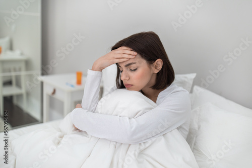 Sick woman sitting in bed, touching head, copy space