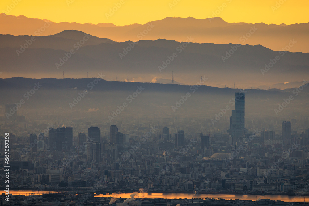 Fototapeta premium Haze layer over city by river and mountains with orange sunrise glow
