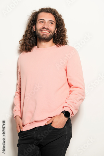 Portrait of curly young man smiling and hands in pockets. Isolated on white.