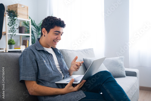 Hispanic teenager boy sitting on couch and having video call or live streaming on laptop. Learning and working from home concept.