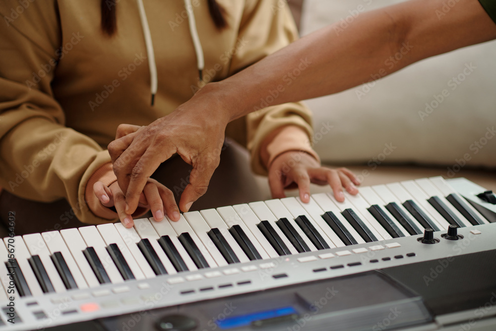 Obraz premium Teacher putting hand of student on synthesizer when explaining how to play chords