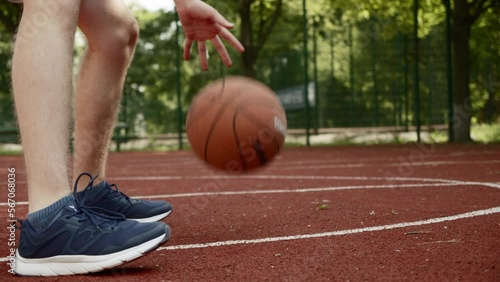 Footage of a teenager dribbling on an outdoor court, during a bright and sunny summer day. Video of a white caucasian teen training to play basketball.
