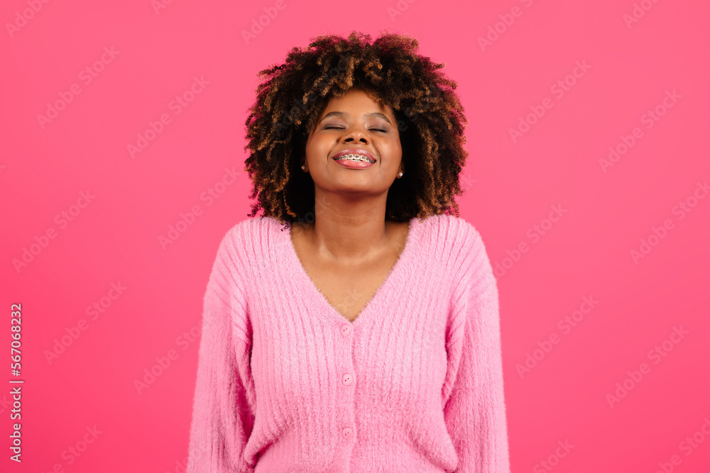 Fototapeta premium Satisfied young black curly lady with braces and closed eyes inhales deeply, enjoys freedom, raises her head