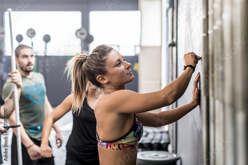 Athlete woman writing down exercises on the gym blackboard making plan for training