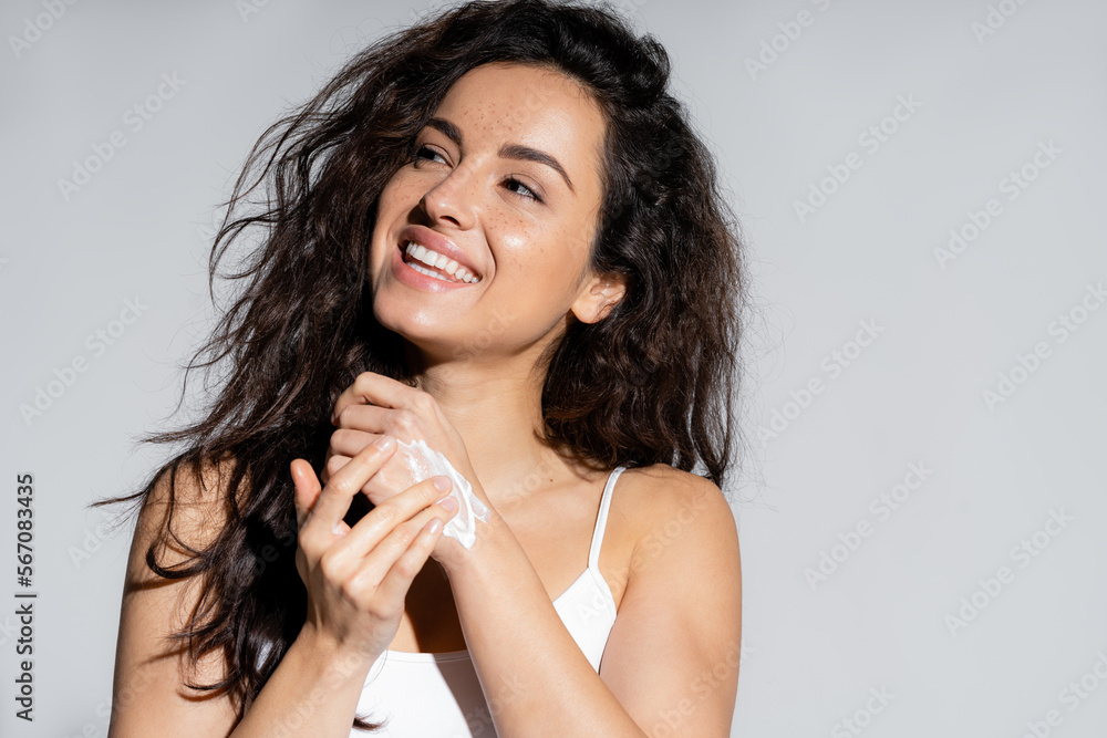 Positive freckled woman applying hand cream isolated on grey. Positive freckled woman applying hand cream isolated on grey.
