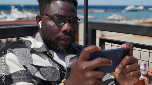 african american guy is watching video on smartphone screen, educational webinar in internet