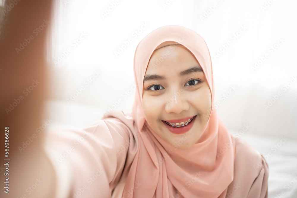 Asian Muslim woman lying at the bed Using Smartphone selfie and smiling, with her smile dental care. Asian Muslim woman lying at the bed Using Smartphone selfie and smiling, with her smile dental care.