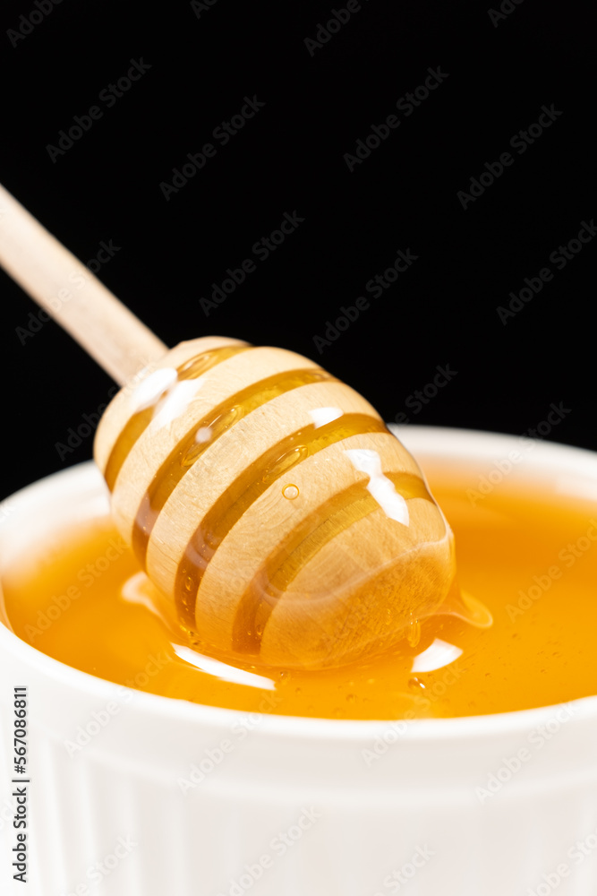 Honey in a white ceramic bowl with a wooden spoon on a black background. Honey in a white ceramic bowl with a wooden spoon on a black background.