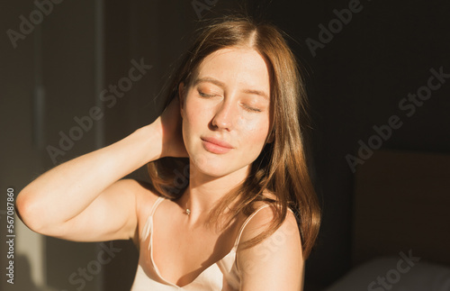 Portrait woman waking up in her bed, she is smiling and stretching. Happy young woman greets new sunny day