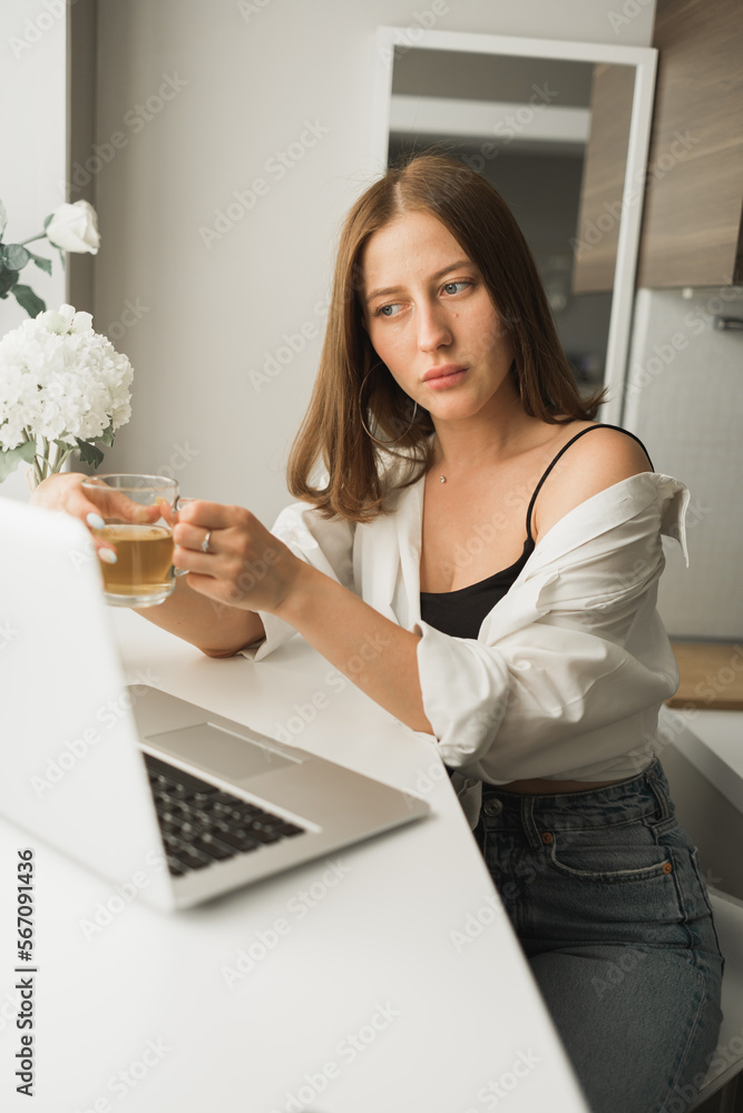 Close up of young pretty woman drinking tea while break after typing and browsing online on laptop working on computer while sitting in cozy room alone. Distance learning and work with break for Close up of young pretty woman drinking tea while break after typing and browsing online on laptop working on computer while sitting in cozy room alone. Distance learning and work with break for