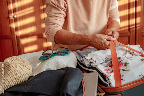 Closeup on senior woman's hands while packing her clothes in a suitcase preparing for the summer vacation trip. Travel preparation concept