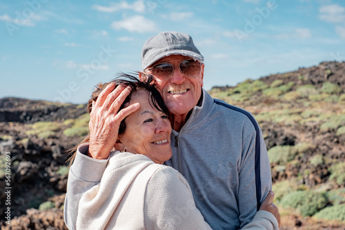 Smiling caucasian senior couple tenderly embraced enjoying sunny day in countryside excursion. Elderly people in vacation or retirement at sea