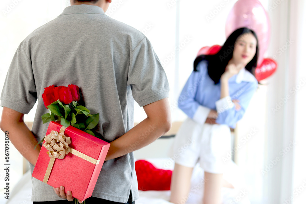 Man hiding red gift box with beautiful red rose bouquet behind back, ready to give Valentine present to lover girlfriend for celebration, couple make surprise, love and happiness. Happy Valentine Day Man hiding red gift box with beautiful red rose bouquet behind back, ready to give Valentine present to lover girlfriend for celebration, couple make surprise, love and happiness. Happy Valentine Day