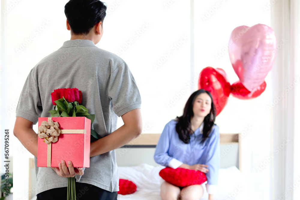 Man hiding red gift box with beautiful red rose bouquet behind back, ready to give Valentine present to lover girlfriend for celebration, couple make surprise, love and happiness. Happy Valentine Day Man hiding red gift box with beautiful red rose bouquet behind back, ready to give Valentine present to lover girlfriend for celebration, couple make surprise, love and happiness. Happy Valentine Day