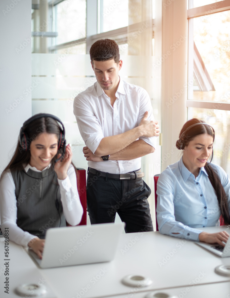 Handsome male mentor teaching, supervising and giving instructions to call centar workers in office Handsome male mentor teaching, supervising and giving instructions to call centar workers in office