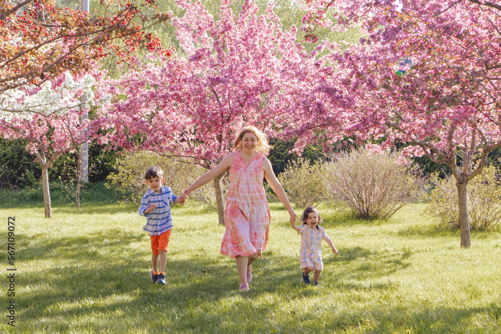 Obraz premium Woman holding hands with children while wallking happily at a park in Spring