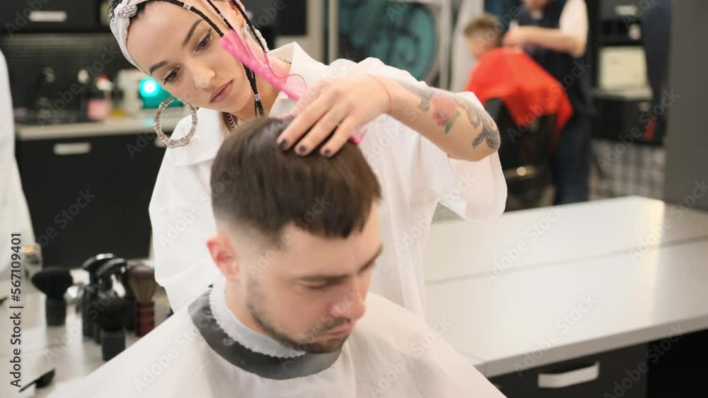 A stylish female hairdresser cuts the hair of a man in a barber shop A stylish female hairdresser cuts the hair of a man in a barber shop