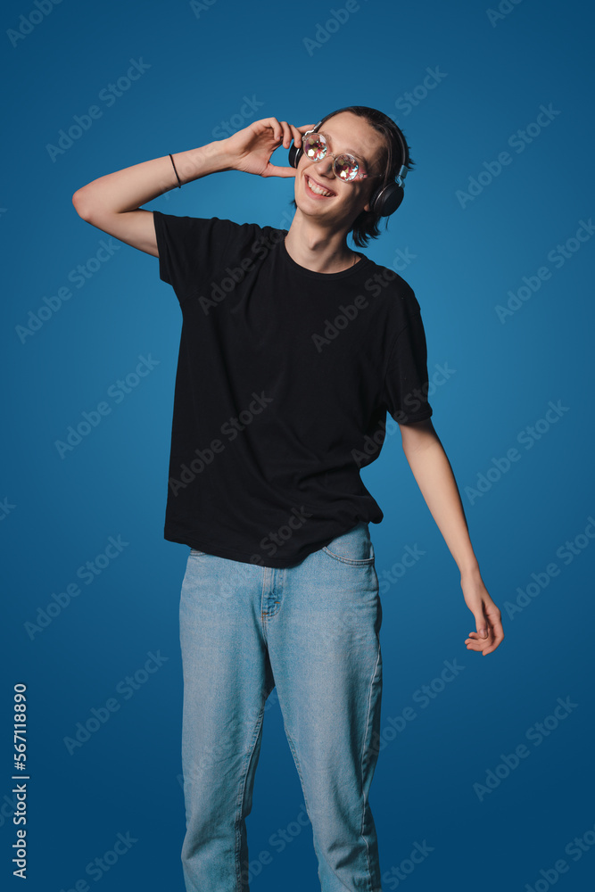 Naklejka premium Young caucasian musician wearing sunglasses in headphones listening to music isolated over blue background. Concept of music, hobby, festival.