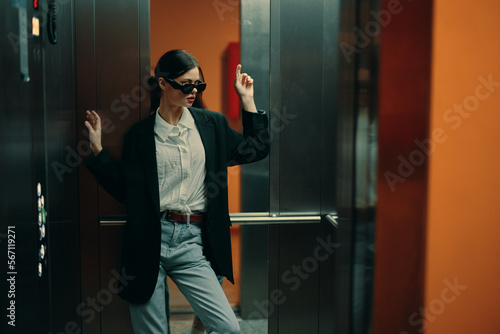 Stylish woman in black jacket and sunglasses posing in elevator, fashion model, dark cinematic light and color, glamor vintage