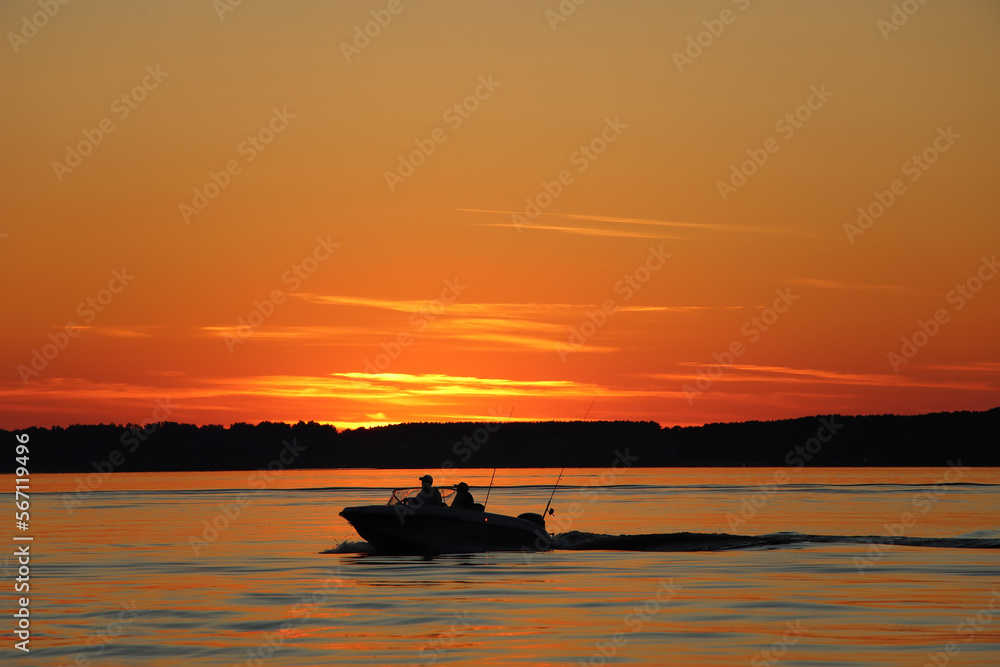 Silhouette of two fisherman on the boat. Beautiful sunset on the background.
