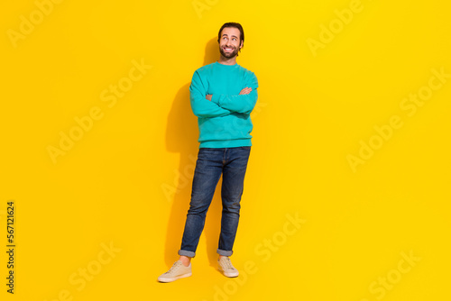Full length photo of dreamy funny man wear turquoise clothes arms crossed looking empty space isolated yellow color background