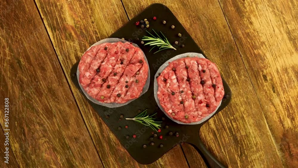 Raw meat burger cutlets, with spices and rosemary sprigs rotate on kitchen board. Tasty cutlets preparation on domestic kitchen. Copy space. Top view. Close up. Raw meat burger cutlets, with spices and rosemary sprigs rotate on kitchen board. Tasty cutlets preparation on domestic kitchen. Copy space. Top view. Close up.