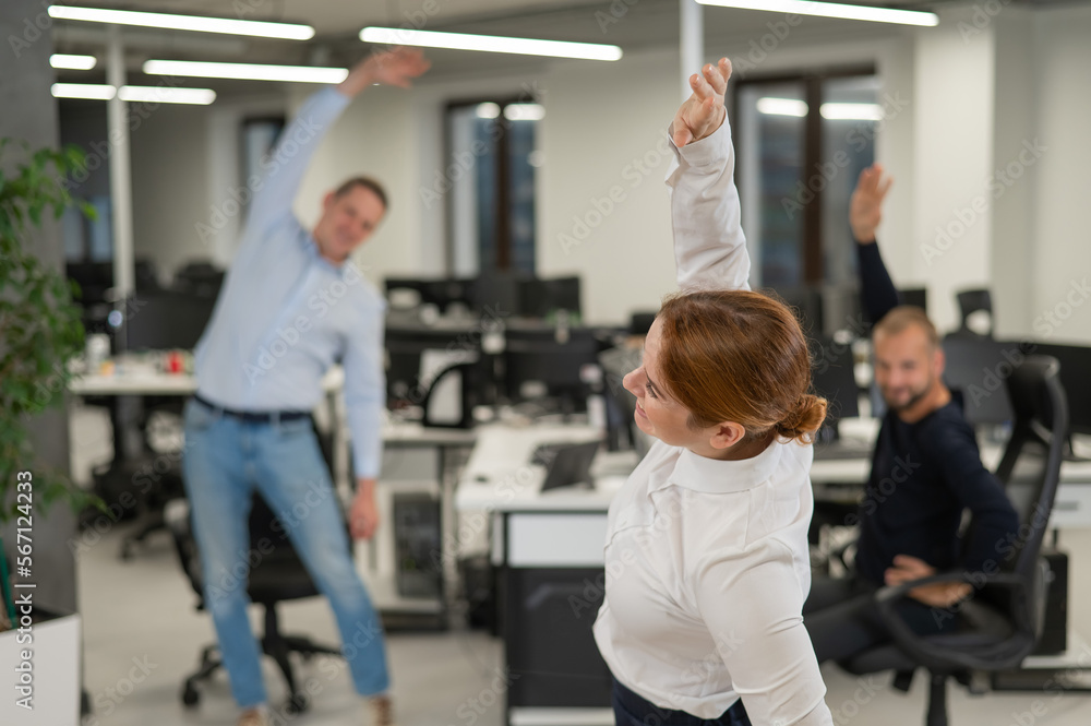 Three office workers warm up during a break. Employees do fitness exercises at the workplace. Three office workers warm up during a break. Employees do fitness exercises at the workplace.