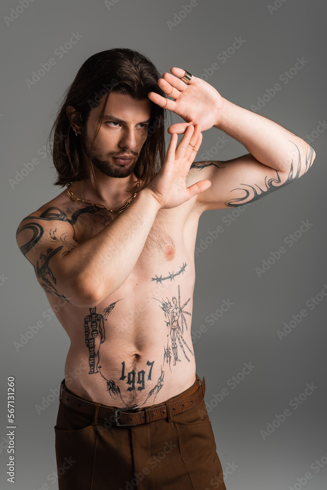 Fototapeta premium Bearded long haired model with tattoo on torso posing isolated on grey.
