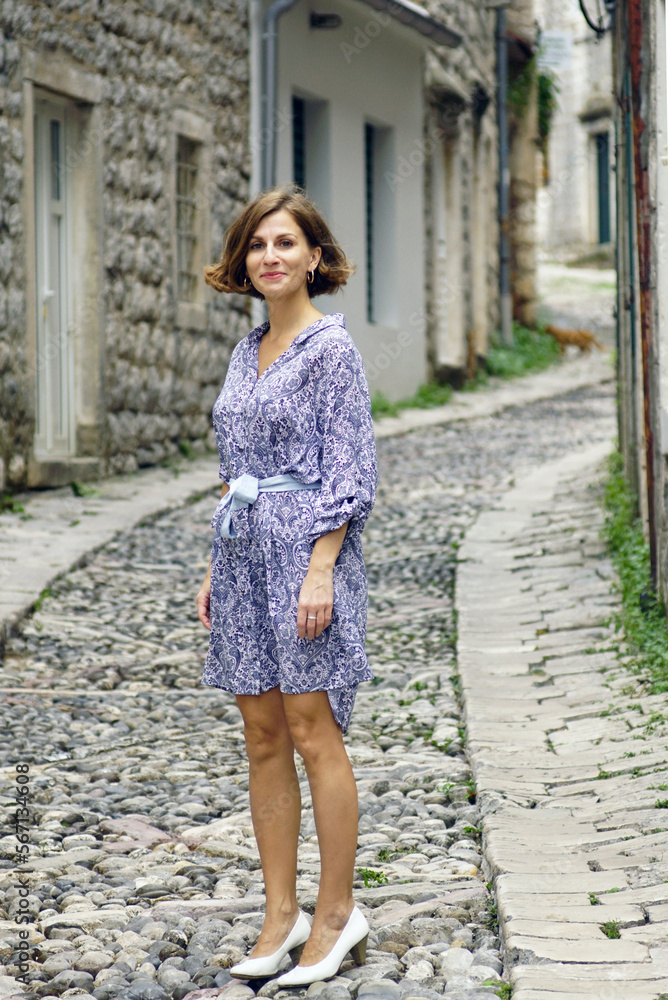 Full-length portrait of a young smiling woman standing on an upward-sloping stone-paved road in an old European city Full-length portrait of a young smiling woman standing on an upward-sloping stone-paved road in an old European city