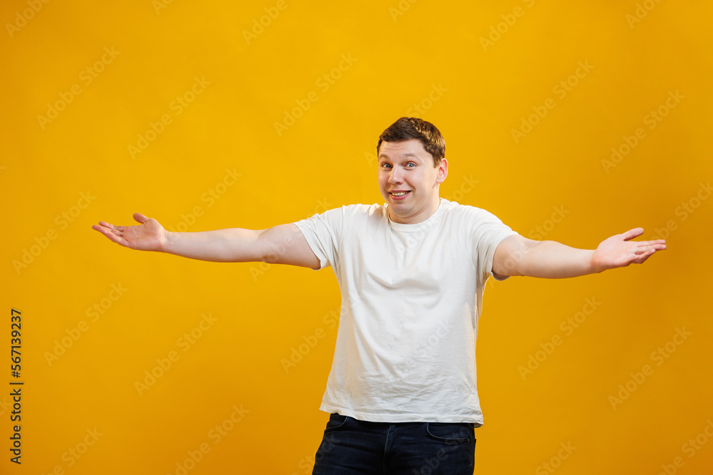Handsome positive man wearing white t-shirt spread his hands to the sides and doesn't know what to do standing over yellow studio background Handsome positive man wearing white t-shirt spread his hands to the sides and doesn't know what to do standing over yellow studio background