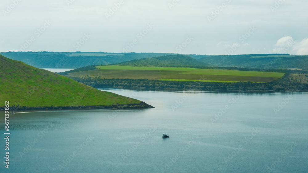 Beautiful widescreen panorama 16*9 of  Bakota in Tovtry national nature park, Ukraine, in summer, with green hills, river Dniester and overcast sky, a small boat in the centre, part of touristic trail