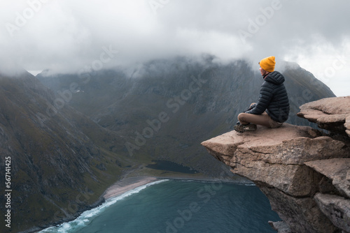 Lone man meditating on a rock at the edge of the void in winter. Man sitting on top of Ryten in Norway, Lofoten islands. Success, self confidence and trust symbol