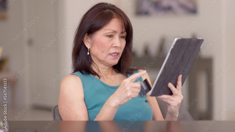 Attractive mature woman relaxing shopping online with tablet and e-commerce credit card sitting in leisure home living room chair Attractive mature woman relaxing shopping online with tablet and e-commerce credit card sitting in leisure home living room chair
