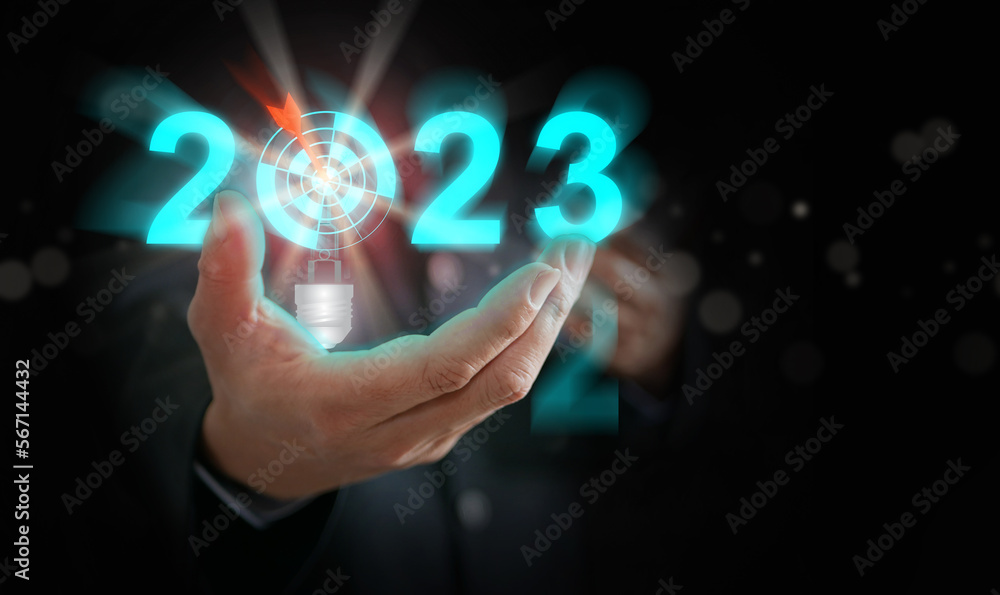Businessman's hand holding the year 2023 with light blub, dart, and target. Starting new year, business, project, path, goal, or life. Control, manage, choose, and decide by and for yourself. Businessman's hand holding the year 2023 with light blub, dart, and target. Starting new year, business, project, path, goal, or life. Control, manage, choose, and decide by and for yourself.