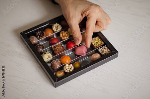 Assorted Valentine’s Day chocolates. Chocolate chocolates of different colors and shapes. Man’s hand reaches for heart candy. Box of sweets