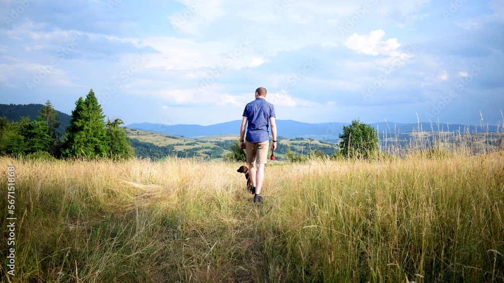 Man on a walk with the dog in the sunny summer day. Trekking with a dog in the mountains