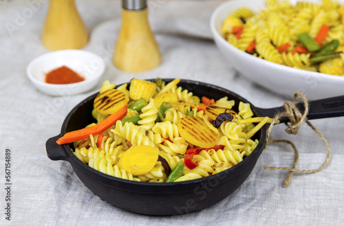 Pasta with vegetables and spices in a cast-iron frying pan.