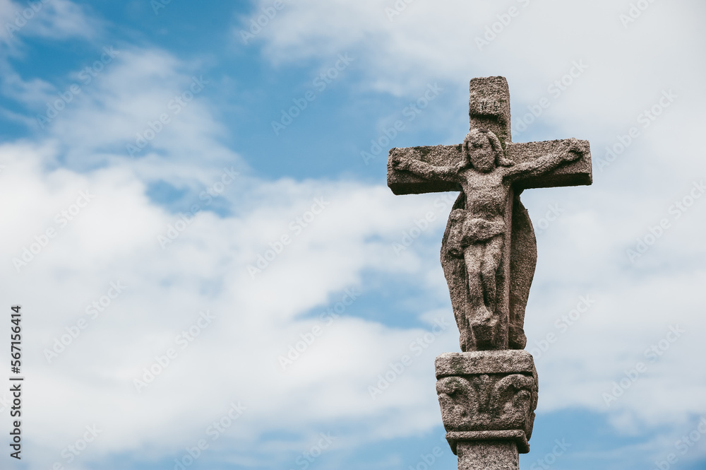 Ancient white stone crucifix with Jesus in cloudy blue sky
