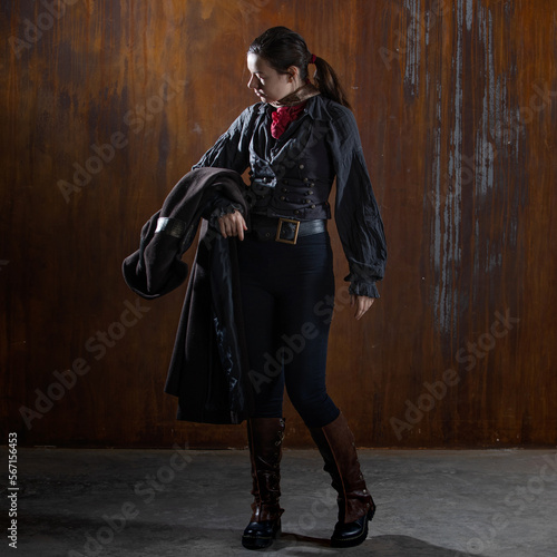 Fantasy steampunk action heroine in a long coat. A woman in a retro fantasy outfit on the background of a textured rusty wall