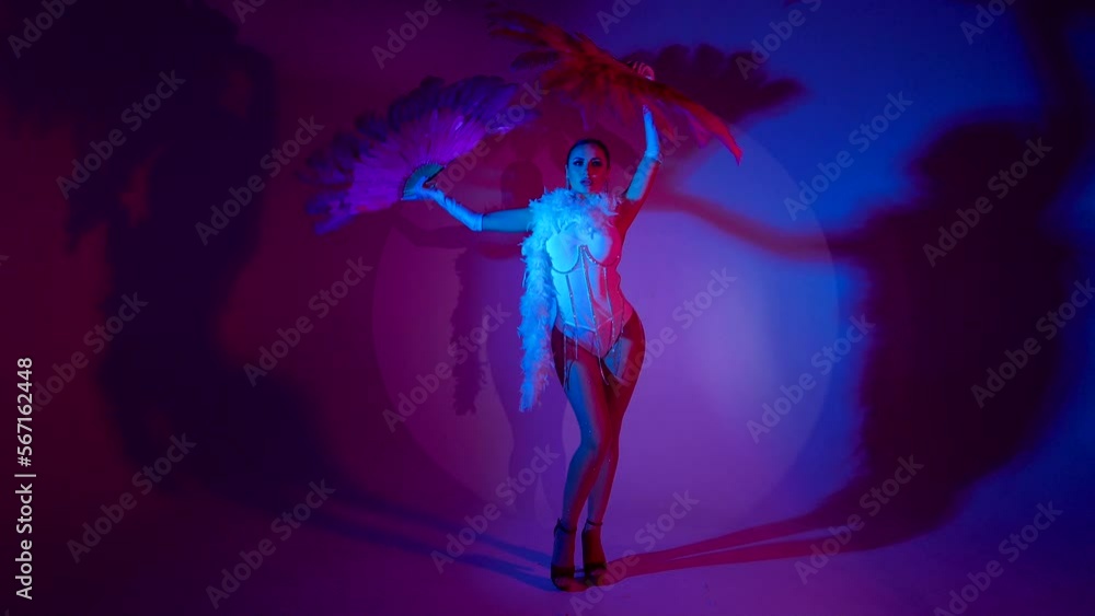 Brunette in a white dance bodysuit with a bright evening make-up with a white boa with large fans with colored red and blue lighting Brunette in a white dance bodysuit with a bright evening make-up with a white boa with large fans with colored red and blue lighting