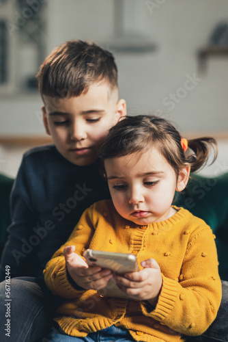 Kids using technology at home. Brother and sisters using mobile device