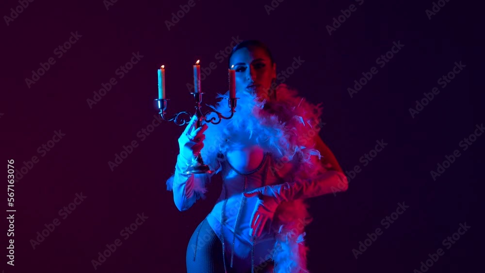 Brunette in a white dance bodysuit with a bright evening make-up with a white boa with a candelabra and three burning candles with colored red-blue lighting Brunette in a white dance bodysuit with a bright evening make-up with a white boa with a candelabra and three burning candles with colored red-blue lighting