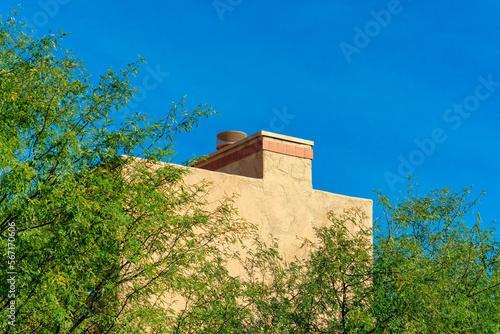 Decorative chimney with light adobe beige cement and orange tiles with front or back yard trees and plants