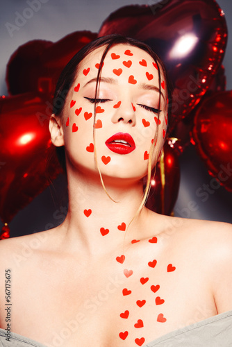 Portrait of a woman with heart stickers on her face. Fashion photo of artistic professional makeup, woman with red lips on the background of balloons. Love and feelings.