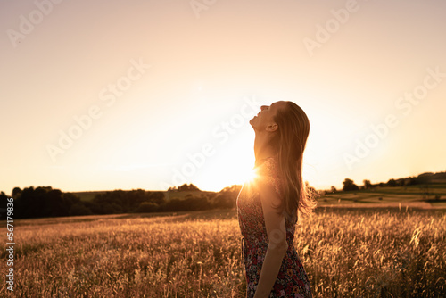 Canvas-taulu Joyful young beautiful woman standing in a field at sunset looking up to the sky