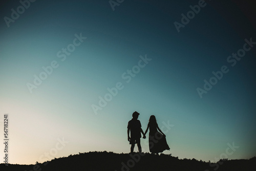 Silhouette of brother and sister standing on sand dune holding hands photo