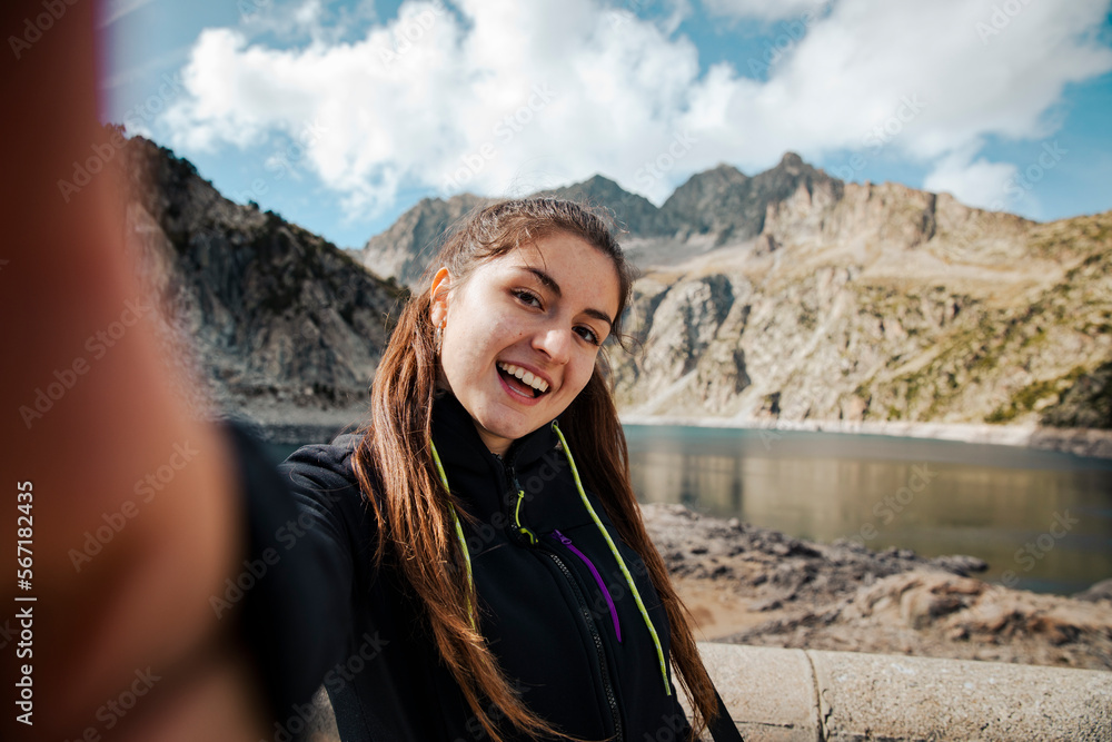 Girl taking a selfie while smiling with a lake in the background Girl taking a selfie while smiling with a lake in the background