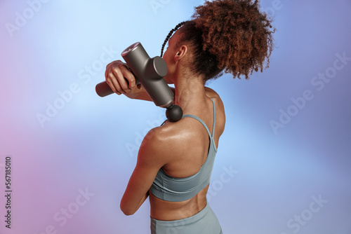 Foto Woman use massage gun machine rehab after muscle workout standing on studio back