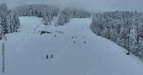 Many skiers and snowboarders skiing down on snowy mountainsides slopes in mountains at ski resort in winter. Family and friends have fun on fresh snow sliding. Bjelasnica mountain.  photo