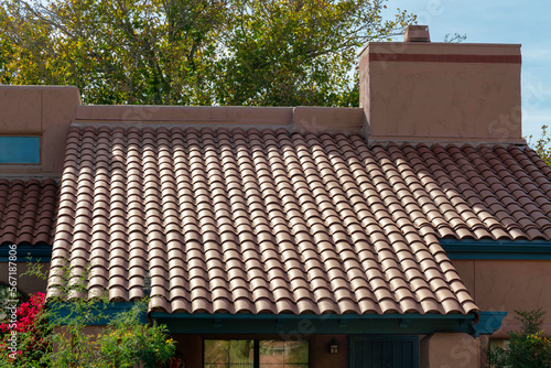 Low angle and horizontal roof on adobe style house with visible chimney and red tiles in late afternoon desert sun
